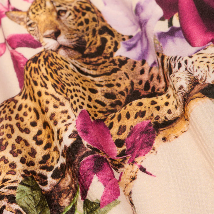 A close-up of the Violet String Bikini Bottom highlights its smooth, cream-colored fabric adorned with a rose leopard print and purple flowers, showcasing intricate spots and floral patterns.