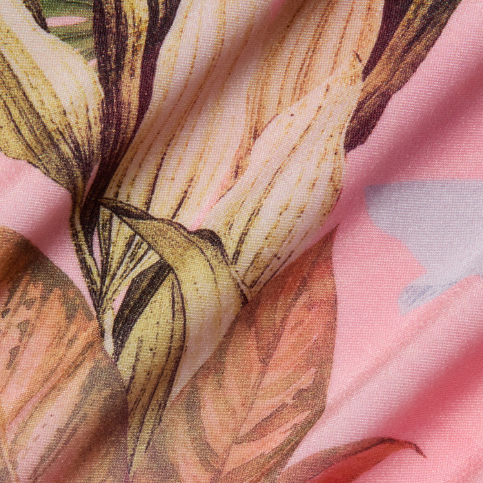 Close-up of the Violet String Bikini Bottom in pink fabric, featuring a palm leaf print combined with large yellow and orange flowers and green leaves, showing visible folds and texture.