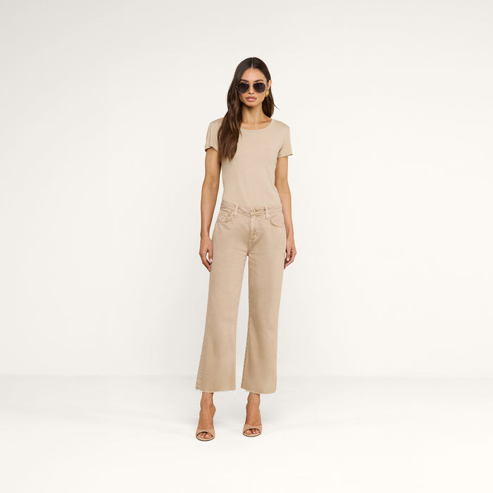 A woman wearing sunglasses, a neutral tan t-shirt, the Wanda Cropped Wide-Leg Jean, and beige heels stands against a plain white background.
