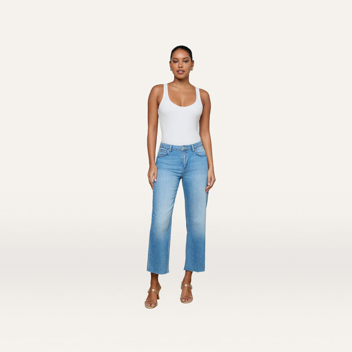A woman stands against a plain background, wearing a white tank top, tan heeled sandals, and the Wanda Cropped Wide-Leg Jean in light blue all-cotton denim.
