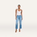 A woman stands against a plain background, wearing a white tank top, tan heeled sandals, and the Wanda Cropped Wide-Leg Jean in light blue all-cotton denim.