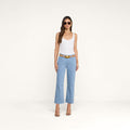 A woman wearing sunglasses, a white tank top, the Wanda Cropped Wide-Leg Jean with a brown belt, and heeled sandals stands against a plain white background.