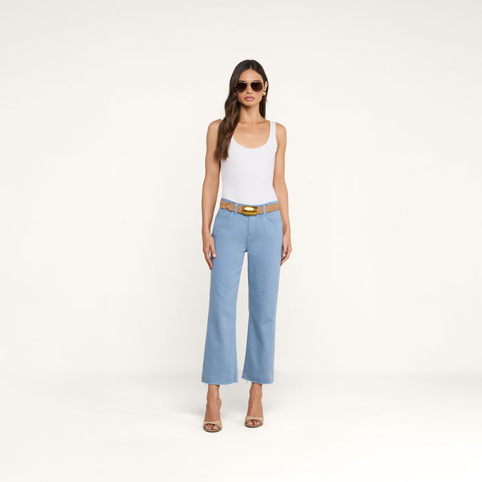 A woman wearing sunglasses, a white tank top, the Wanda Cropped Wide-Leg Jean with a brown belt, and heeled sandals stands against a plain white background.
