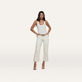 A woman stands against a plain background, wearing a white tank top, open-toe heels, and the Wanda Cropped Wide-Leg Jean in an ecru wash with a belt, her hands resting on her hips.
