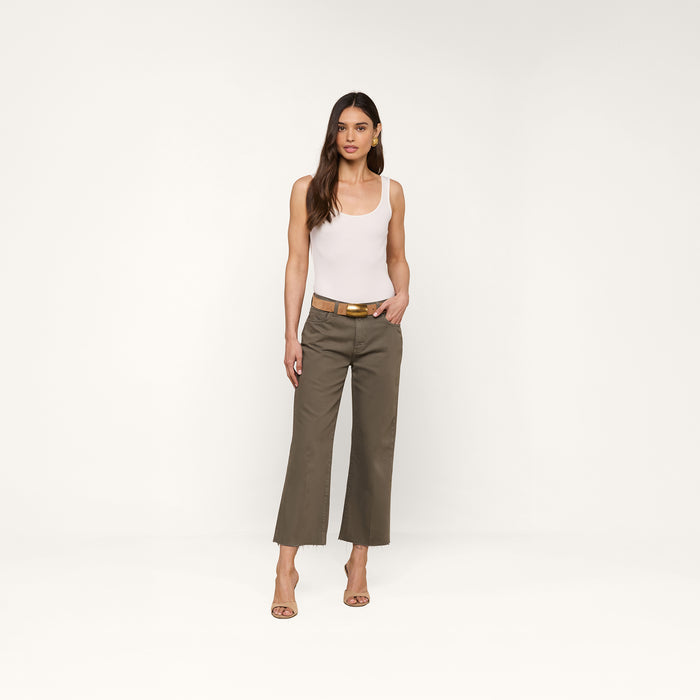 A woman stands facing forward, wearing a white sleeveless top, the Wanda Cropped Wide-Leg Jean in olive green that channels effortless Parisian style, a brown belt, and beige heels against a plain white background.