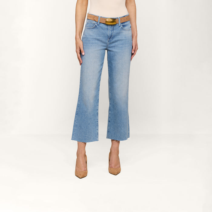 A person wearing the Wanda Cropped Wide-Leg Jean in a light blue wash, styled with a brown belt and tan heels, standing against a plain white background.