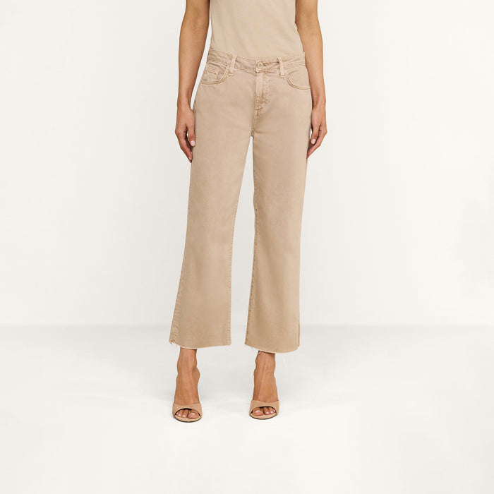 A person stands against a plain white background, wearing the Wanda Cropped Wide-Leg Jean in beige paired with open-toed heels. They have on a neutral tan sleeveless top, and their arms are relaxed at their sides.