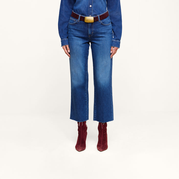A person wearing a featherweight denim shirt, the Wanda Cropped Wide-Leg Jeans with a belt, and burgundy heeled boots stands against a plain white background.