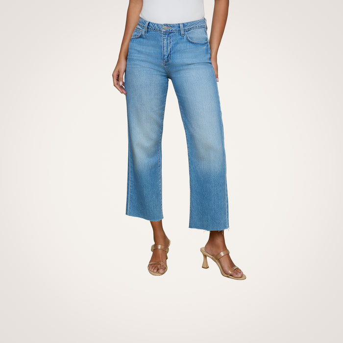 Wearing the Wanda Cropped Wide-Leg Jean in light blue all-cotton denim and tan heeled sandals, the person stands against a plain white background with their upper body partially out of frame.