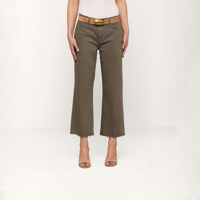 Wearing the Wanda Cropped Wide-Leg Jean in olive green with a frayed hem, a tan belt, a white top, and beige open-toed heels, this person stands against a plain white background, embodying Parisian style.