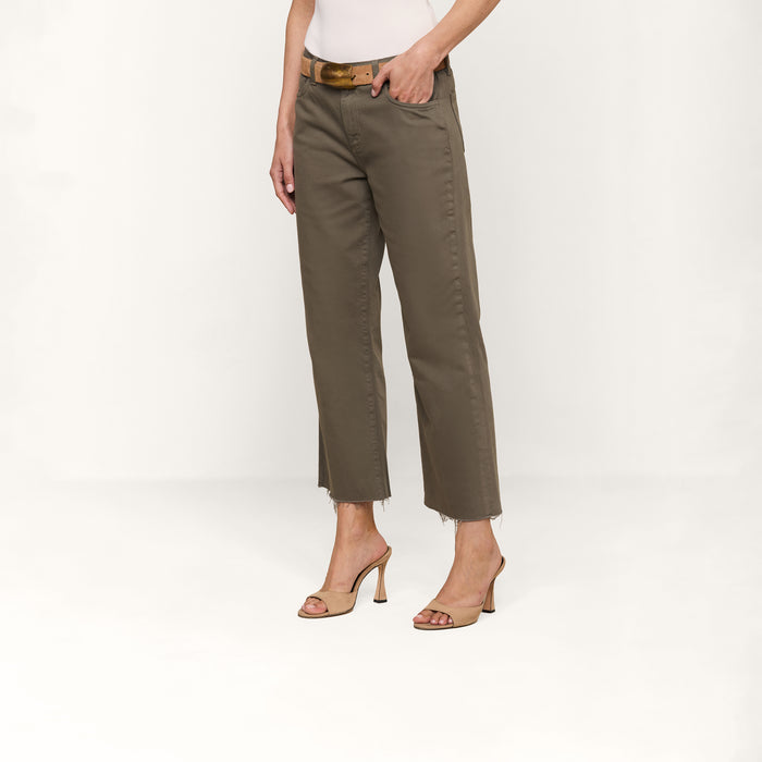 Wearing the Wanda Cropped Wide-Leg Jean in olive green with frayed hems, a beige belt, and nude heeled sandals, this person stands against a plain white background for a chic Parisian style look.
