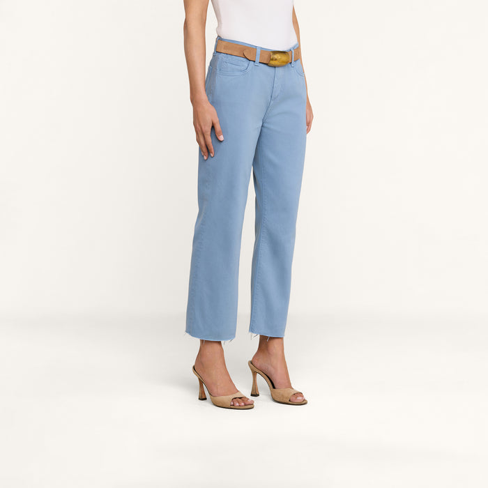 A person wearing the Wanda Cropped Wide-Leg Jean in light blue, a tan belt, a white sleeveless top, and tan high-heeled sandals stands against a plain white background.