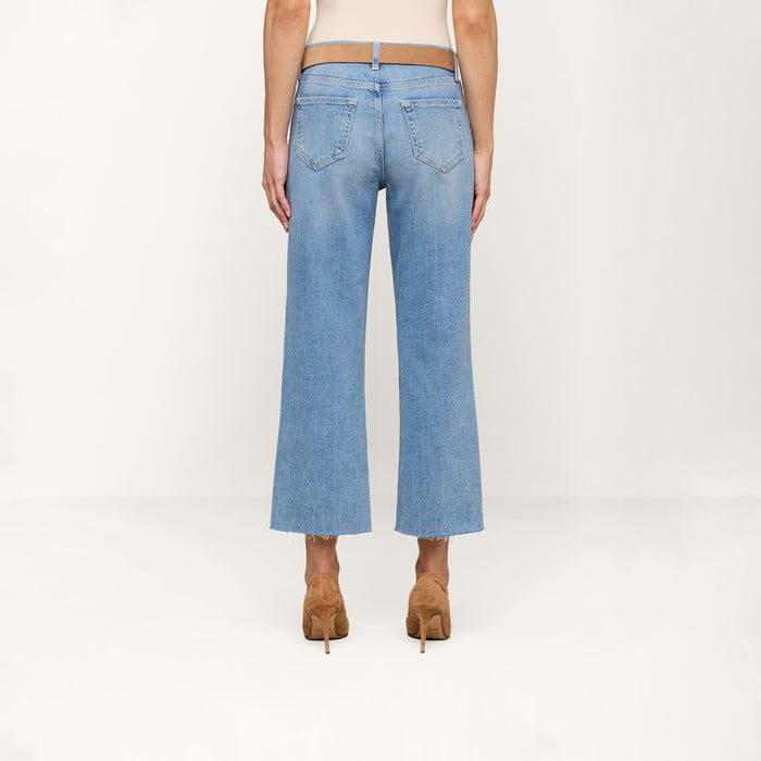 A person stands facing away against a plain white background, wearing the Wanda Cropped Wide-Leg Jean in a light blue wash with a cropped length and two back pockets, paired with tan high heels.