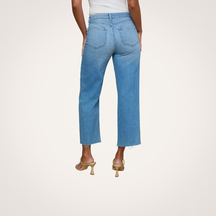A person is seen from behind, standing against a plain white background, wearing the Wanda Cropped Wide-Leg Jean—light blue, high-waisted jeans crafted from 100 cotton denim—and beige heeled sandals.