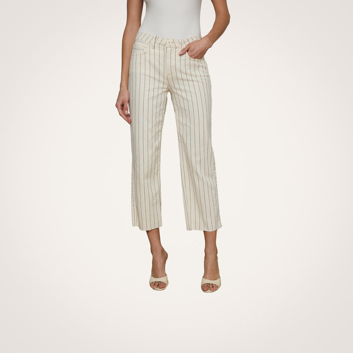 A woman stands against a plain light background, her left hand tucked in her pocket, wearing the Wanda Cropped Wide-Leg Pant in a cream shade with thin nautical stripes, paired with a white sleeveless top and open-toed heels.