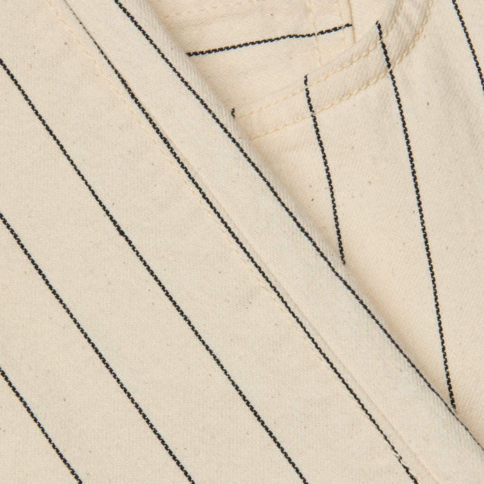 Close-up of the Wanda Cropped Wide-Leg Pant in beige cotton twill with black vertical pinstripes in a nautical stripe pattern, showing part of a seam and pocket. The texture of the fabric and stitching details are visible.