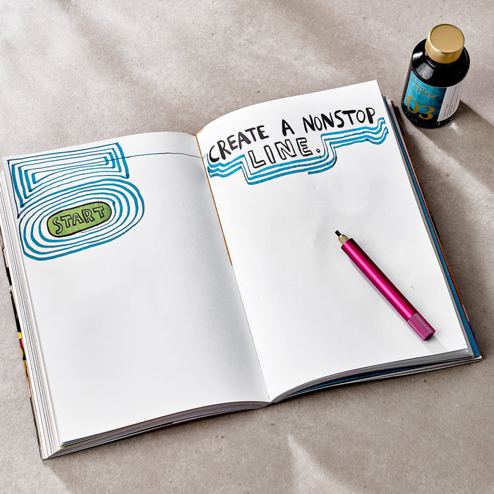 A different spread from Wreck This Journal, showing a creative drawing prompt. The left page displays layered blue and green lines encircling the word “START.” The right page contains the instruction: “CREATE A NONSTOP LINE.” with blue wavy lines drawn underneath. A pink drawing pen and a single bottle of blue-labelled ink rest beside the journal.