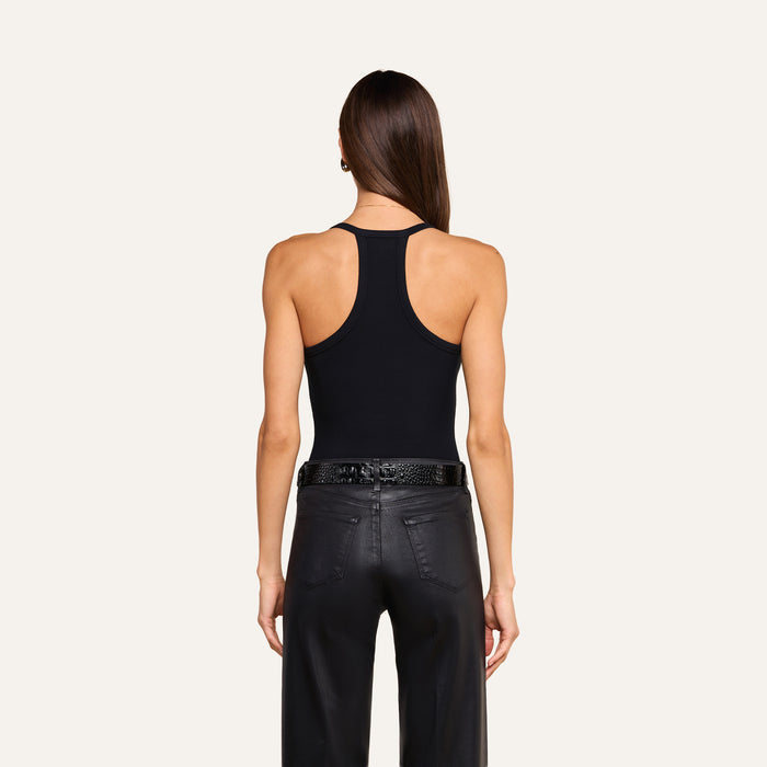 A woman with straight brown hair wearing the Wrenna Racerback Bodysuit, black pants, and a black belt stands facing away on a light background.