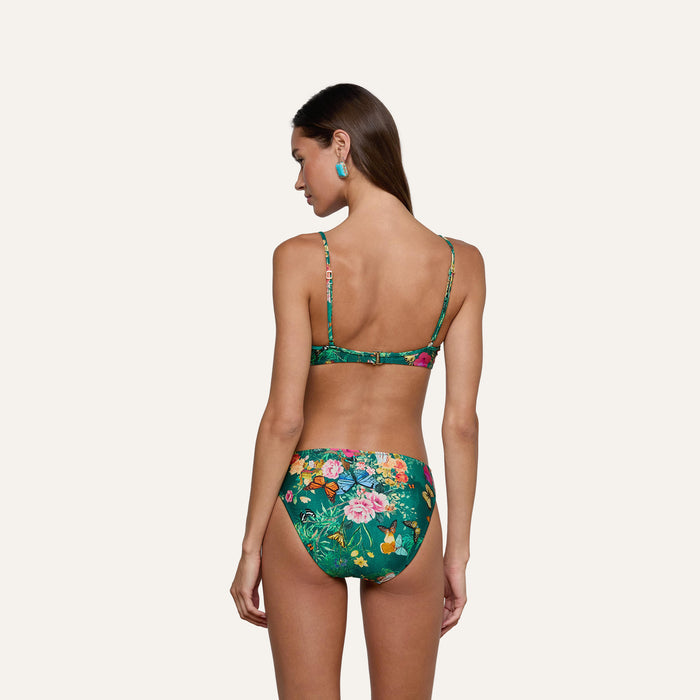 Wearing the Yazmin Bikini Top, a woman with long brown hair and turquoise earrings stands with her back to the camera against a plain light background.