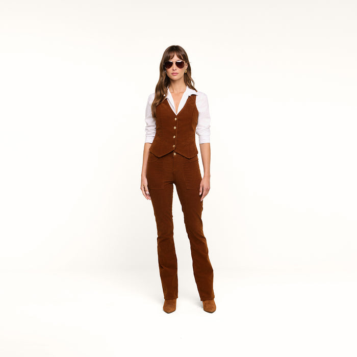 A woman stands facing forward on a plain white background, arms at her sides, wearing sunglasses, a white shirt, the Yelena Vest, and matching casual corduroy brown pants.
