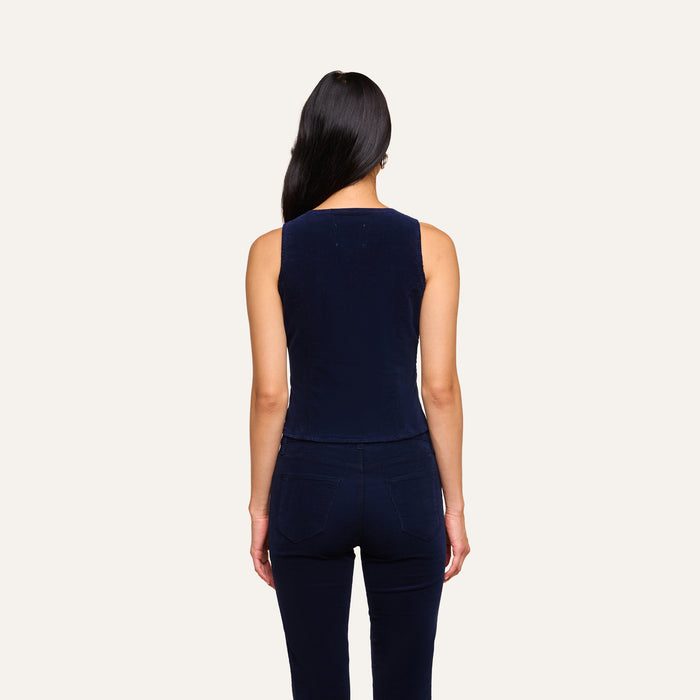 A person with long dark hair, wearing the sleeveless Yelena Vest in navy paired with matching navy pants, stands facing away against a plain light background.