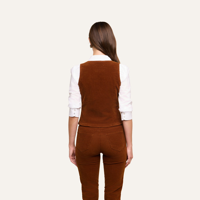 Wearing the Yelena Vest over a white long-sleeve shirt and matching stretch corduroy pants, a woman stands with her straight brown hair falling down her back against a plain light background.