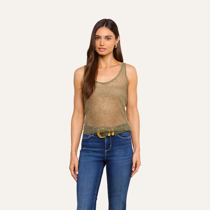 A woman with long brown hair wearing the sheer, sleeveless Zia Tank in gold, paired with blue jeans and a belt, stands facing forward against a plain light background.
